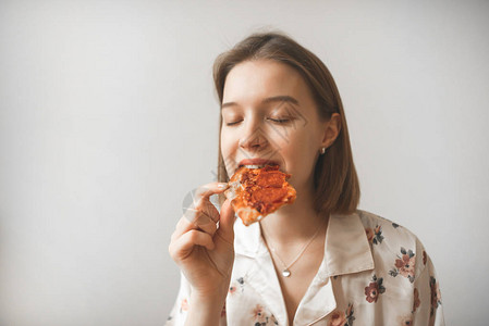 一个有吸引力的女孩的肖像闭着眼睛吃一块比萨饼图片