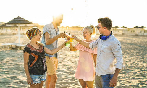 托奇吉在海滩派对上玩得开心的千百年快乐朋友团体在日落时背景