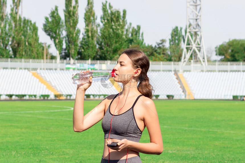 健身赛跑者女人从运动瓶里喝水在体育场训练的能量饮料运动和健康的概念女人拿图片