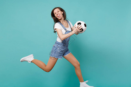 有趣的女足球迷振作起来支持最喜欢的球队拿着足球在蓝色绿松石背景上跳跃图片
