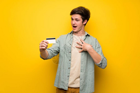 黄墙边的青少年男子拿着信用卡背景图片