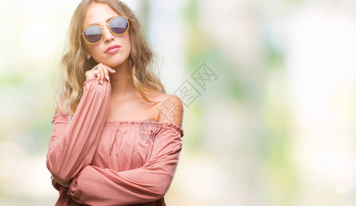 美丽的年轻金发女郎戴着复古太阳镜在孤立的背景下用手托着下巴思考问题图片