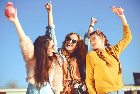 三个女孩在河边对着天空玩得很开心太阳镜的时尚女孩跳跃图片