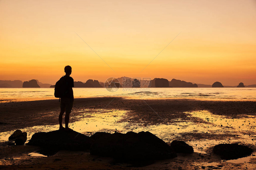 一个站在沙滩上岩石上的男人看着美丽的天空在日出前在泰国彭加省高姚奈KohYa图片