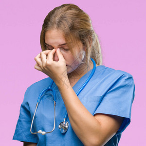 身穿外科医生制服的年轻白人医生女人在孤立的背景下疲惫地揉着鼻子和眼睛图片