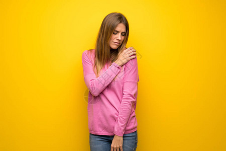 黄色墙上穿着粉色毛衣的妇女因努力而肩部疼痛图片