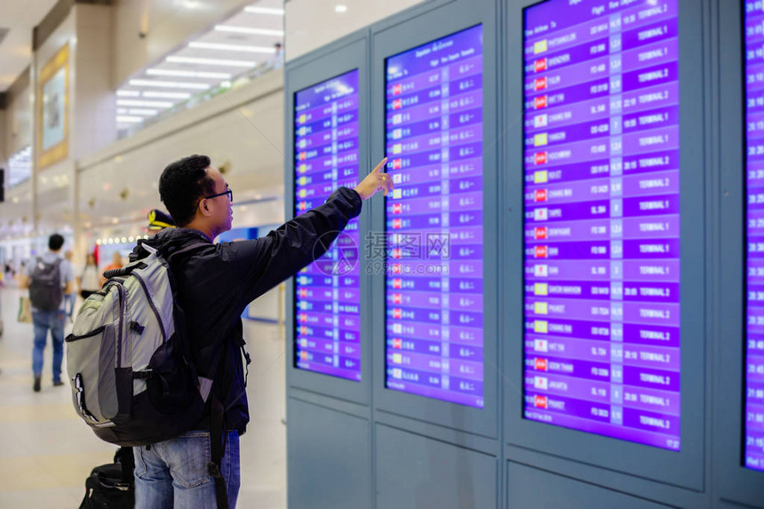 亚洲男子背包旅行者使用智能手机在现代机场的航班信息屏幕上图片