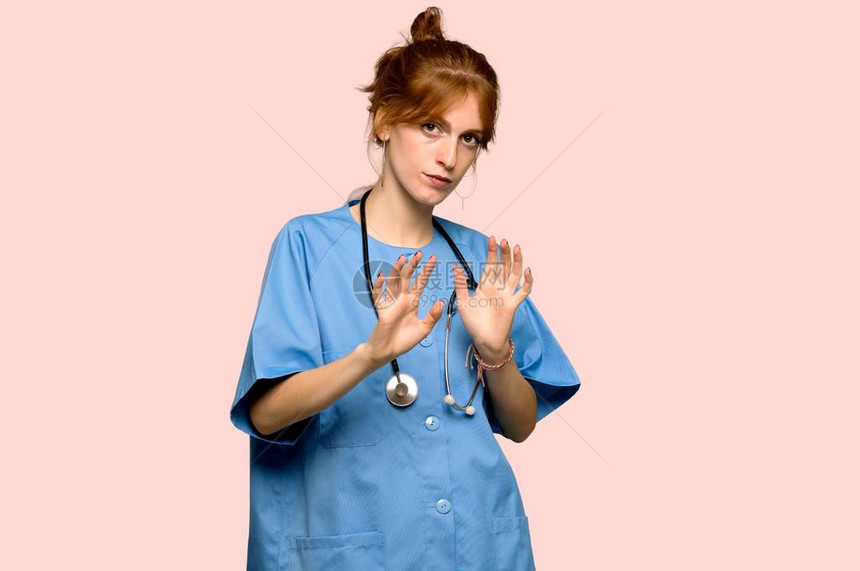 年轻的红发青年护士有点紧张害怕在粉红色背景上把手伸到图片