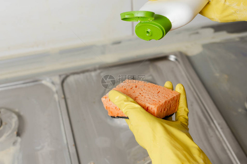 在家将液体肥皂从清洁剂瓶涂抹到海绵上的特写镜头将清洁剂挤出到燃气灶背景上的橙色海绵上图片