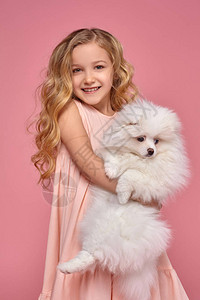 一头金发卷穿着粉色连衣裙的小女孩抱着她的狗图片