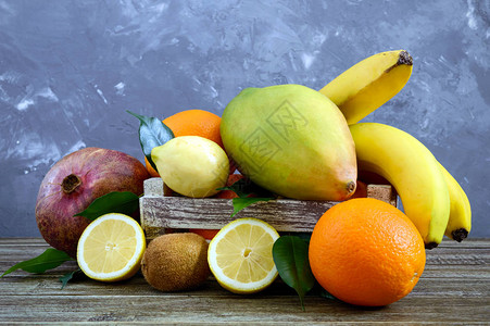 桌上的木箱里有一大堆异国水果香蕉橙子基维石榴芒果图片