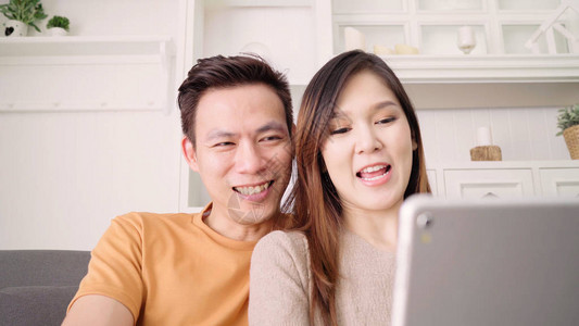 亚洲夫妇在家客厅与朋友使用平板电脑视频通话图片