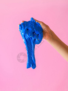 蓝黏液从儿童手上掉落到粉红背景玩具抗压剂发展手动运图片
