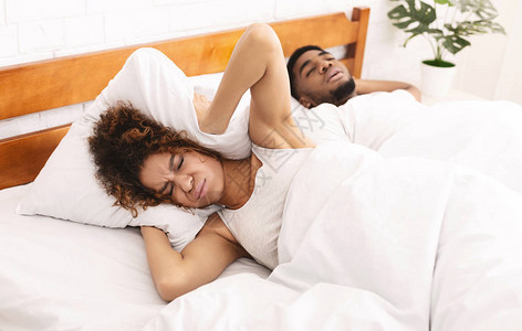 停止打呼的非洲美国女人用枕头遮着耳朵躲在丈夫面前呼图片