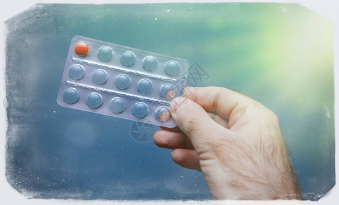 蓝色背景下男手握的药物泡罩包装中最后一个红色药丸的复古框架效应图片