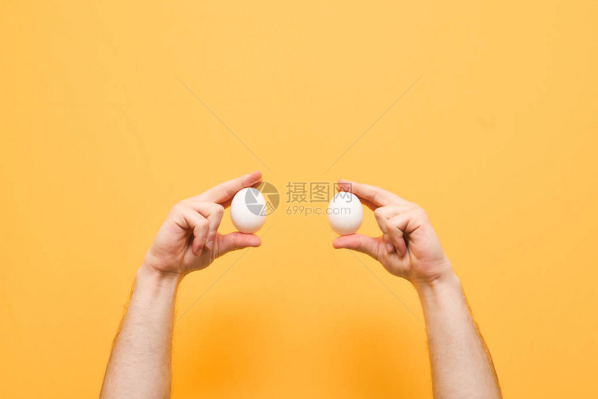 男人的手拿着黄色背景上的两个白鸡蛋带鸡蛋的手被隔离在黄色背景上背图片