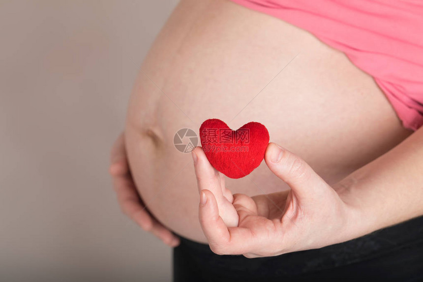怀孕年龄在30至35岁之间的年轻妇女将小红宝石心放在腹部附近图片