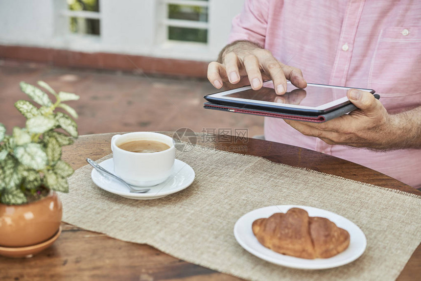 在平板电脑上工作的人和在户外咖啡厅吃早餐的图片