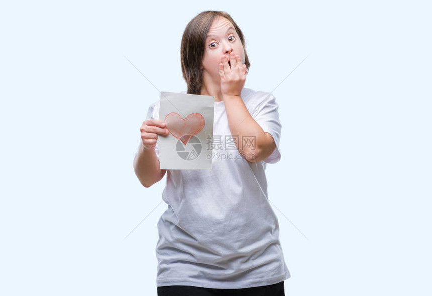 患有唐氏综合症的年轻成年女拿着红心卡在孤立的背景上用手捂住嘴图片