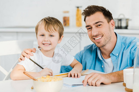 父亲和学龄前儿子在厨房吃早餐时观看图片