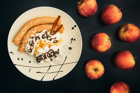 煎饼在盘子上装饰着干酪奶油苹果和巧克力在鸡蛋和红苹果图片