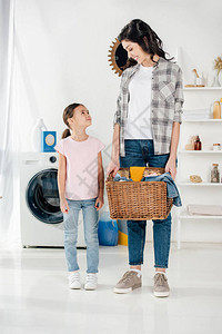 身穿粉红色T恤穿着灰色衬衣和篮子在洗衣房里站在靠近母图片