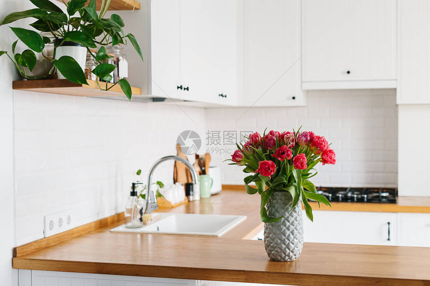 花瓶里的郁金香花束站在厨房的木制台面上斯堪的纳维亚风格的现代白色u形厨房厨房里的架子上放图片