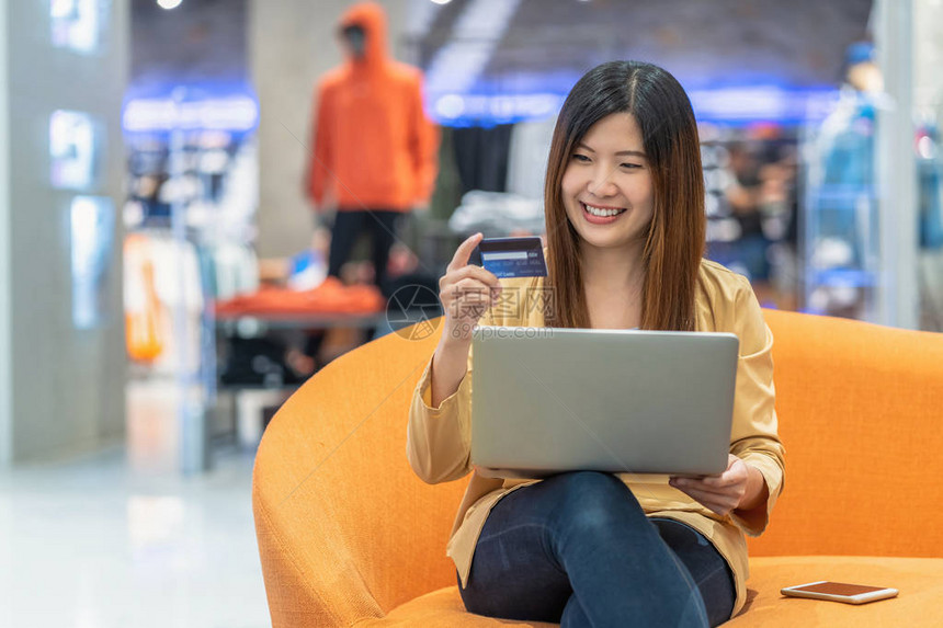 亚洲女使用带手机的信用卡在服装店背景下的百货公司网上购物技术货币钱包和在线支付概念图片