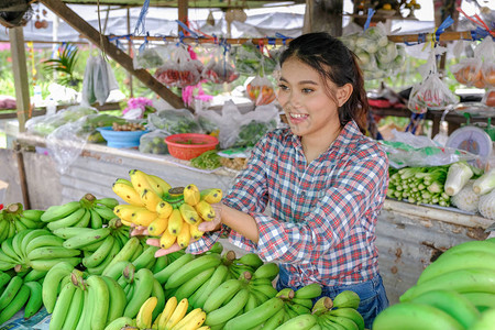 女商人在泰国的一家农村路边商店出售成熟黄色的蔬菜水果和香蕉图片