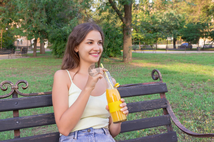 有一瓶新鲜橙汁的年轻美女享受着公园里美好的天图片