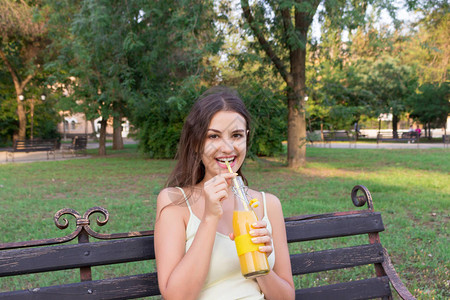 年轻的漂亮女孩正在喝柠檬水从瓶子到吸管的吸管图片