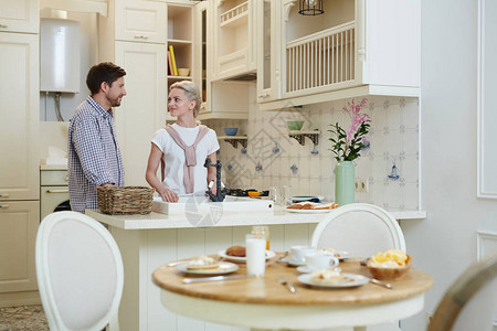 一对身着休闲服的漂亮年轻夫妇微笑着站在厨房柜台图片