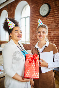 两个穿着生日帽子的快乐年轻女青年和在庆祝节日时看着你在办公图片
