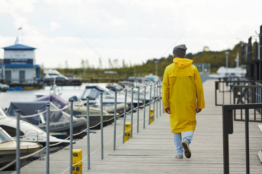看着机动船只和秋天在码头上行走的黄色防水大衣和帽子上的孤单图片