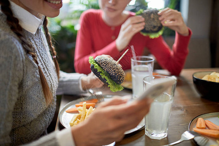 有芝士汉堡的女孩在午餐前用智能手机向朋友传图片