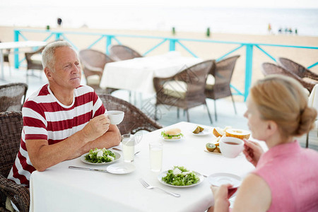 现代老年夫妇在户外餐桌边吃素食午餐和喝图片