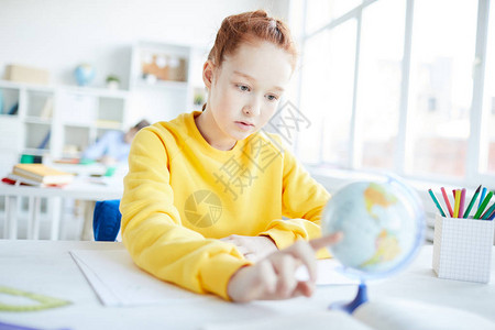 严肃的小女孩坐在书桌旁转身地球模型学习图片