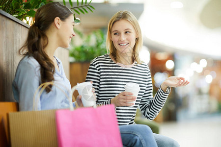 两名友好的随意女孩在购物后在现代商场休息时聊图片