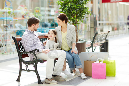 三口的年轻家庭坐在贸易中心的长椅上图片