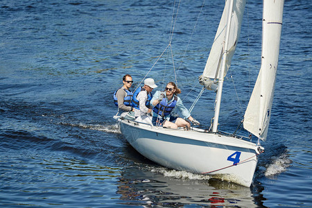 一群戴着太阳镜和救生衣的游艇人坐在帆船甲板上图片