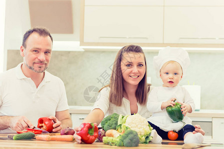 快乐的父母坐在厨房里准备和她们的女婴厨师一起图片