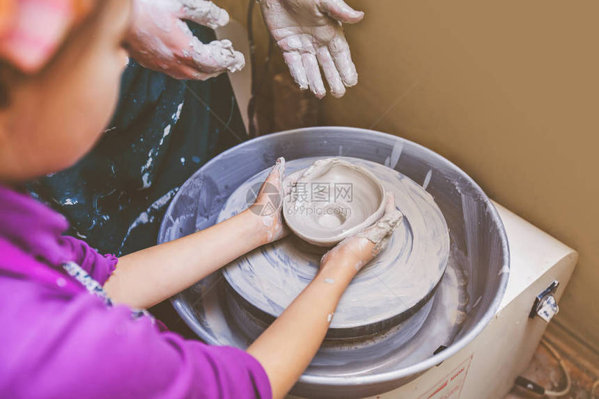 在陶器车轮上塑造粘土的小女孩协助教师参图片