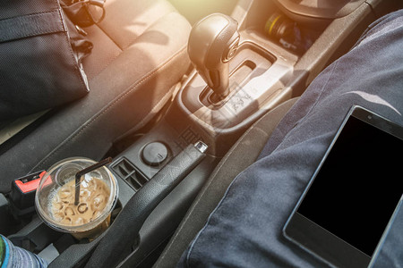 司机用手机咖啡和假日旅行摄像袋的汽车内图片