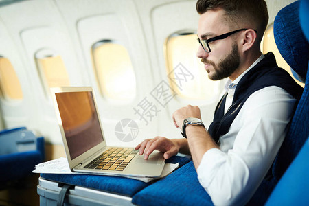 英俊商人在长头等舱飞行期间使用笔记本电脑在飞机上工作时的侧面肖图片