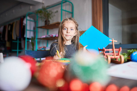 微笑的小女孩在艺术和工艺作室的餐桌旁制作手工制作的圣诞装饰品的肖图片