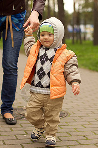 婴儿在妈身后学习在公园里散步可爱的男婴学习走路在母亲帮图片