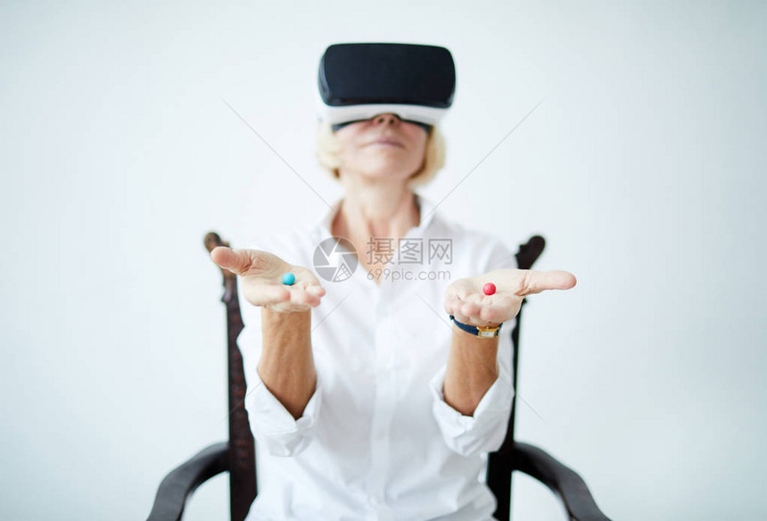 身戴VR头盔和手持两片不同药片的成年妇女肖像图片