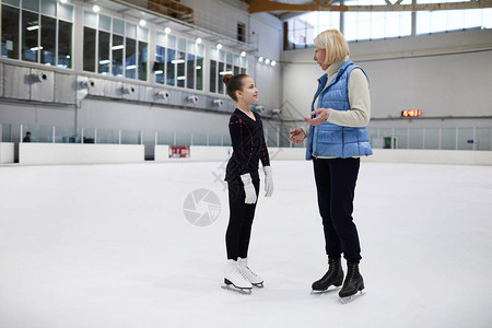 溜冰场花样滑冰练习中成熟女教练与小女孩交谈的全长肖图片