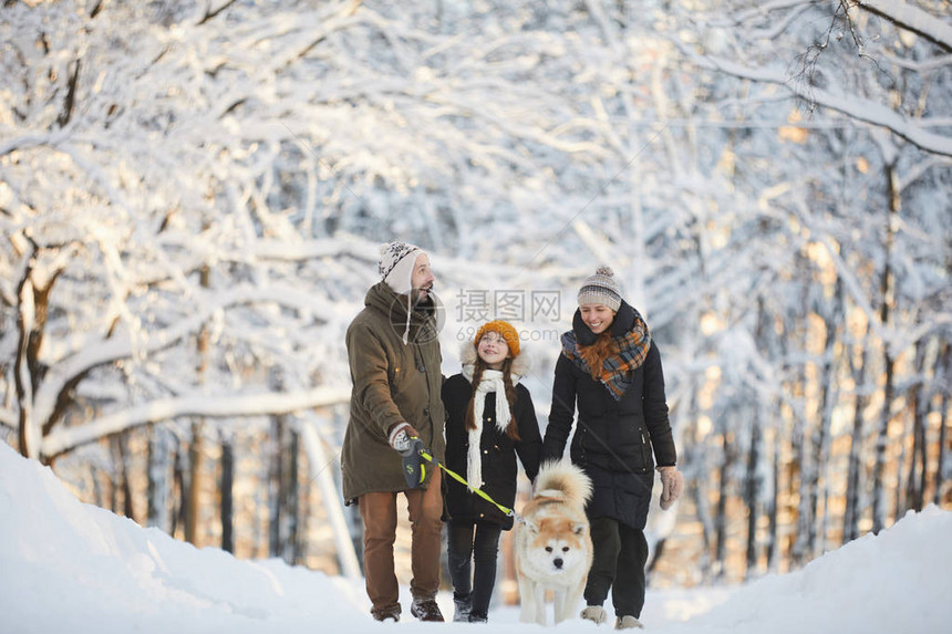 快乐家庭在美丽的冬季森林里与狗一起散步的完整长的肖图片