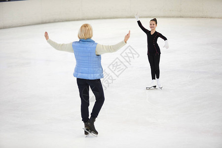快乐女孩的全长肖像在滑冰场上滑雪由女教练指图片